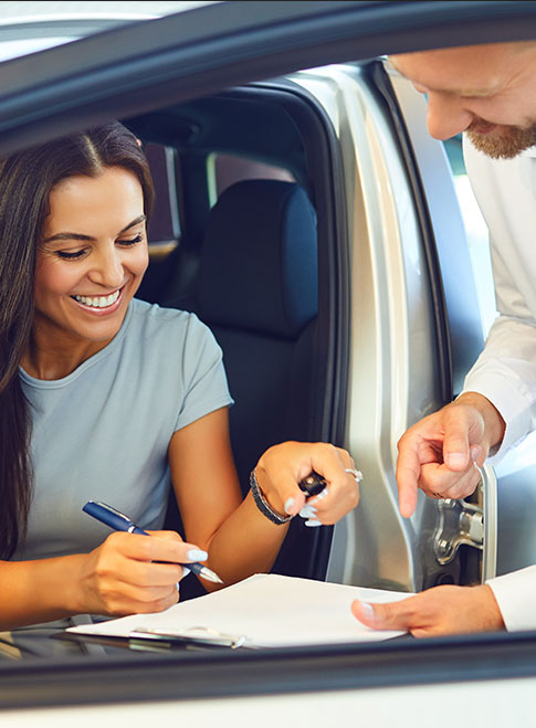 A smiling person signs a document from the open door of a car.