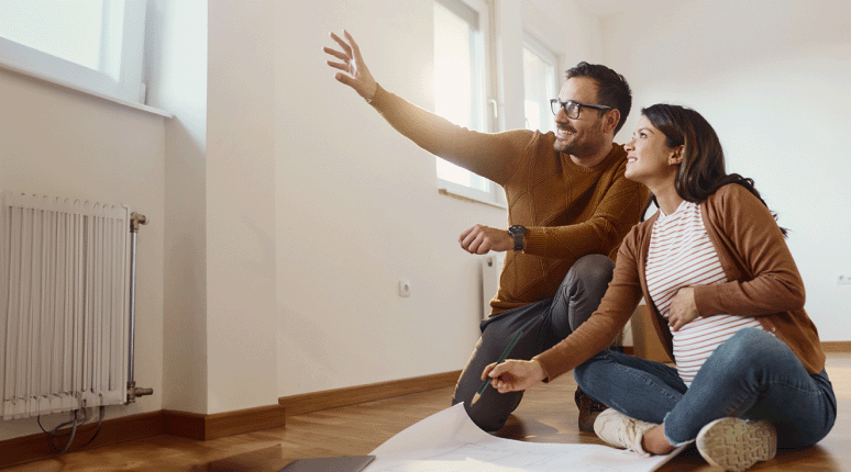 A pregnant wife and her husband consider making changes to their home as they look at their window and their home's floor plan.