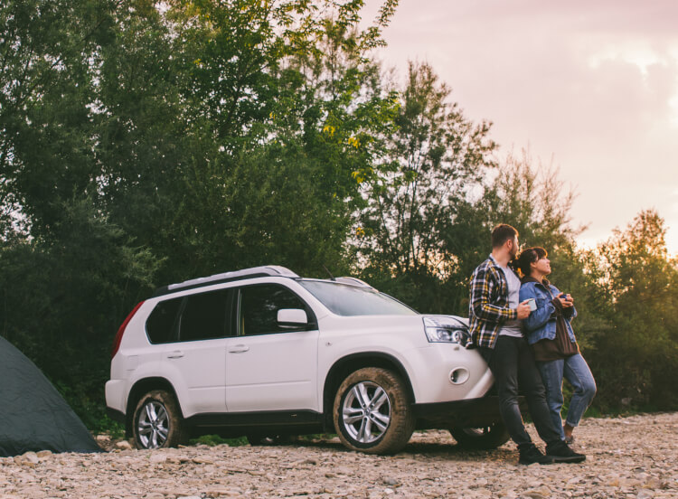 Happy couple feeling gratified, leaning on car with coffees, enjoying the sunrise.