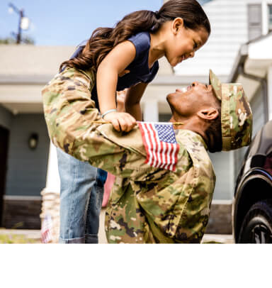 Military dad in fatigues lifting his young daughter up with confidence.