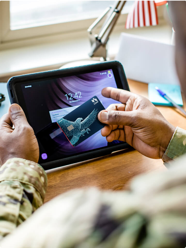 Hands of a USAA member in fatigues banking with debit card and tablet