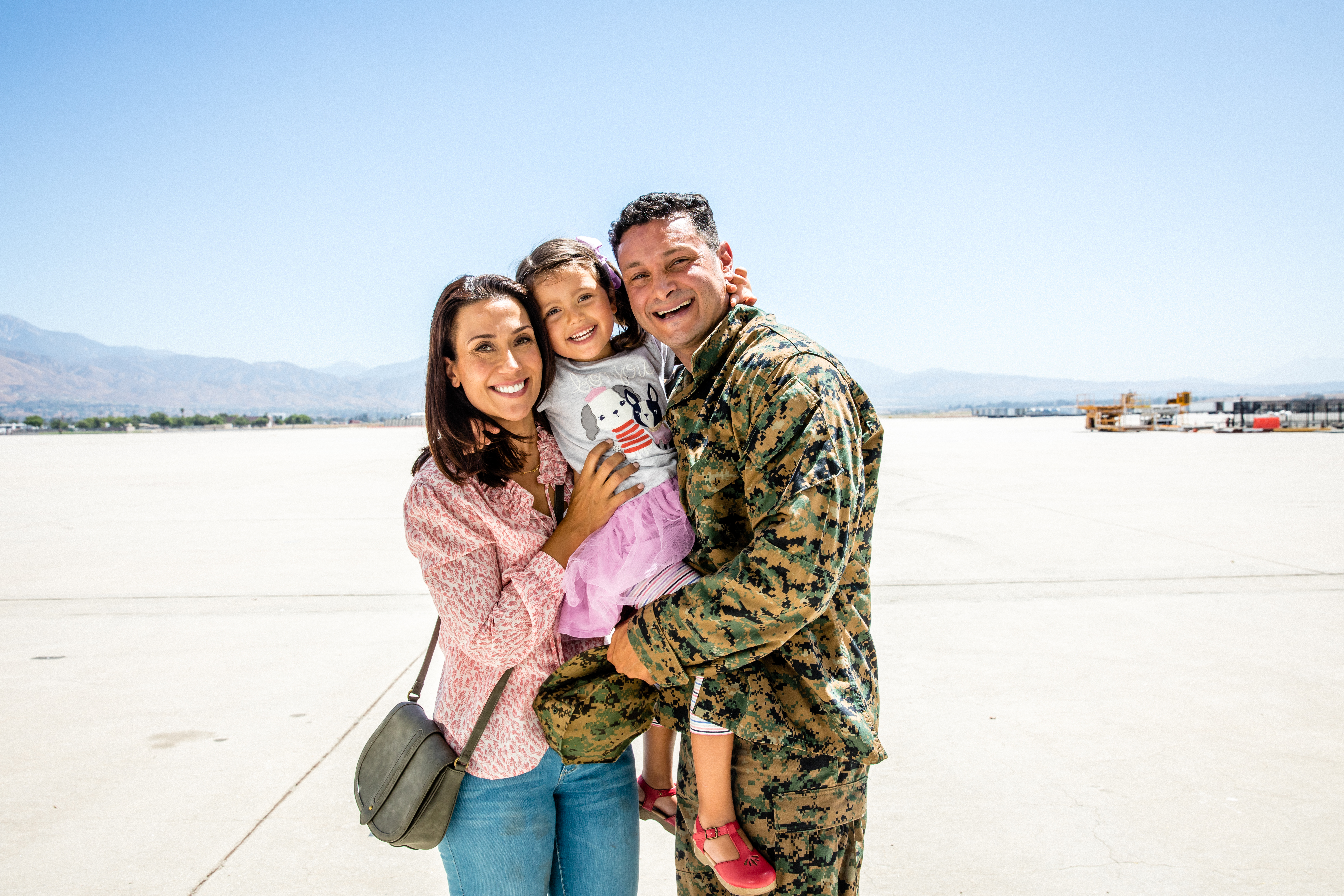 Photo of a military family smiling and hugging as they reunite on an airplane runway.