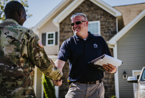 USAA insurance claims professional cheerily shakes hand with an active-duty military member outside his home.