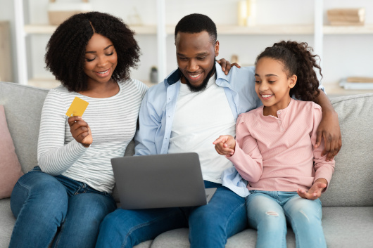 Child telling parents what to purchase online. Dad holding computer, mom holding credit card.