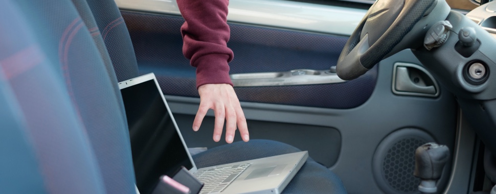 A person reaches their hand inside a car window to steal a laptop.