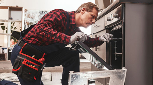 A man wearing a toolbelt looks at a stove