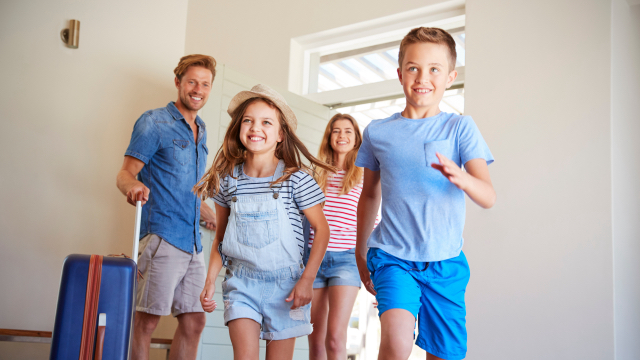 An excited family walks into a home with a suitcase.