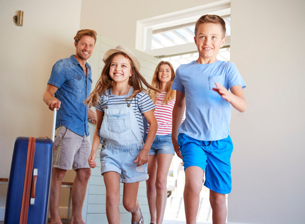 An excited family walks into a home with a suitcase.