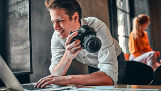 A person holds a camera and types on a laptop.