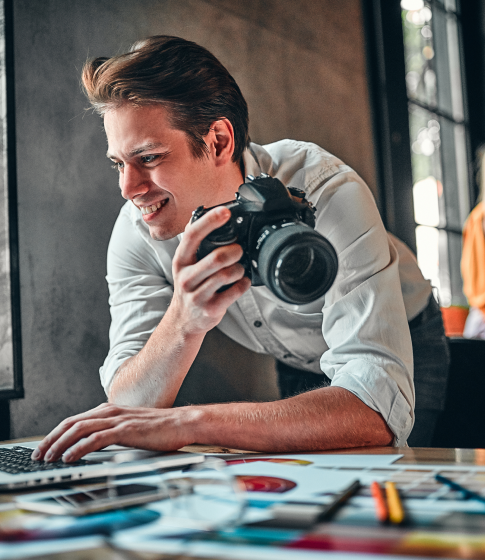 A person holds a camera and types on a laptop.