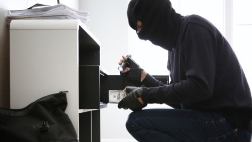  A thief in a mask looks for stuff to steal after breaking into a home.