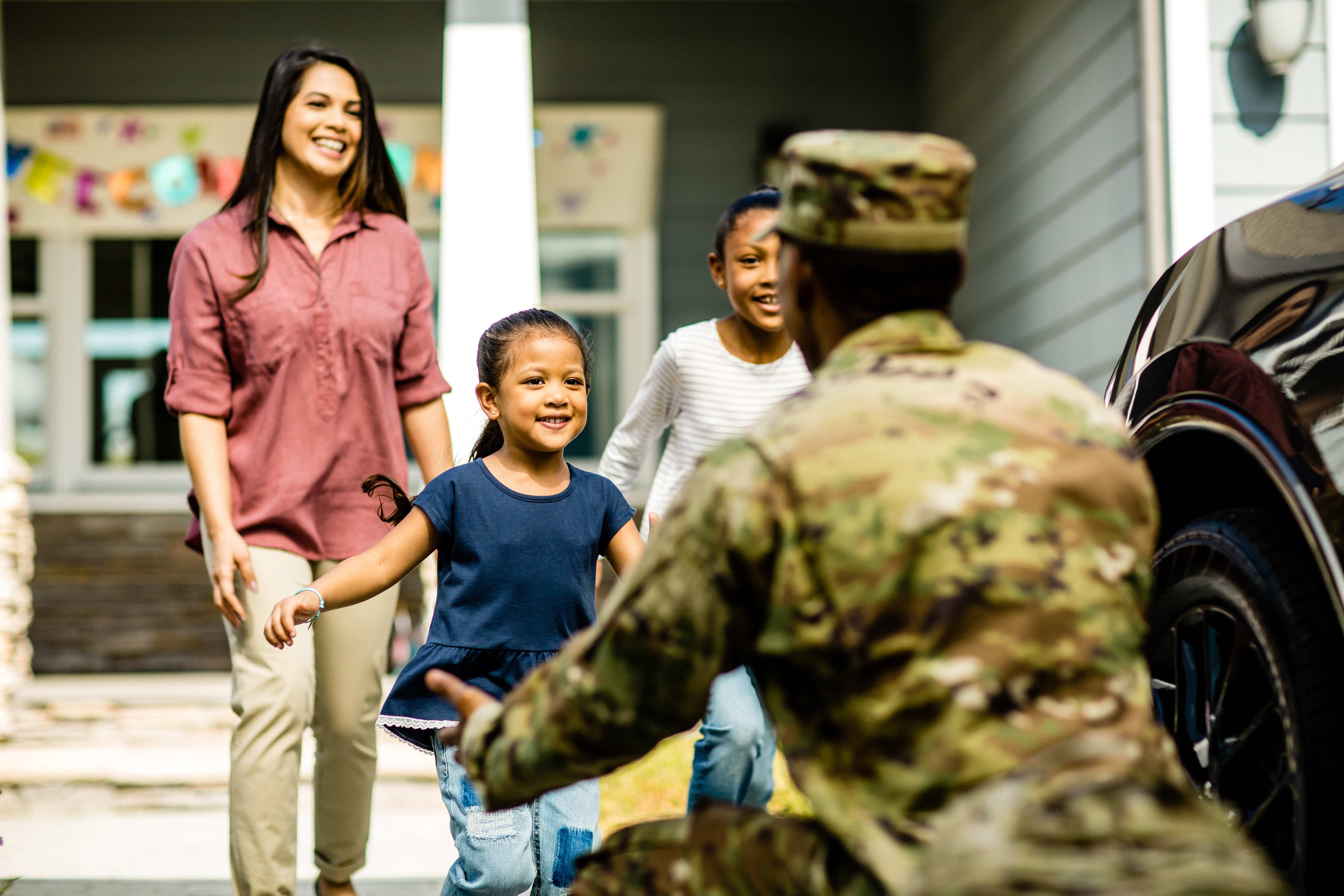 A smiling family runs to hug a military member in uniform.