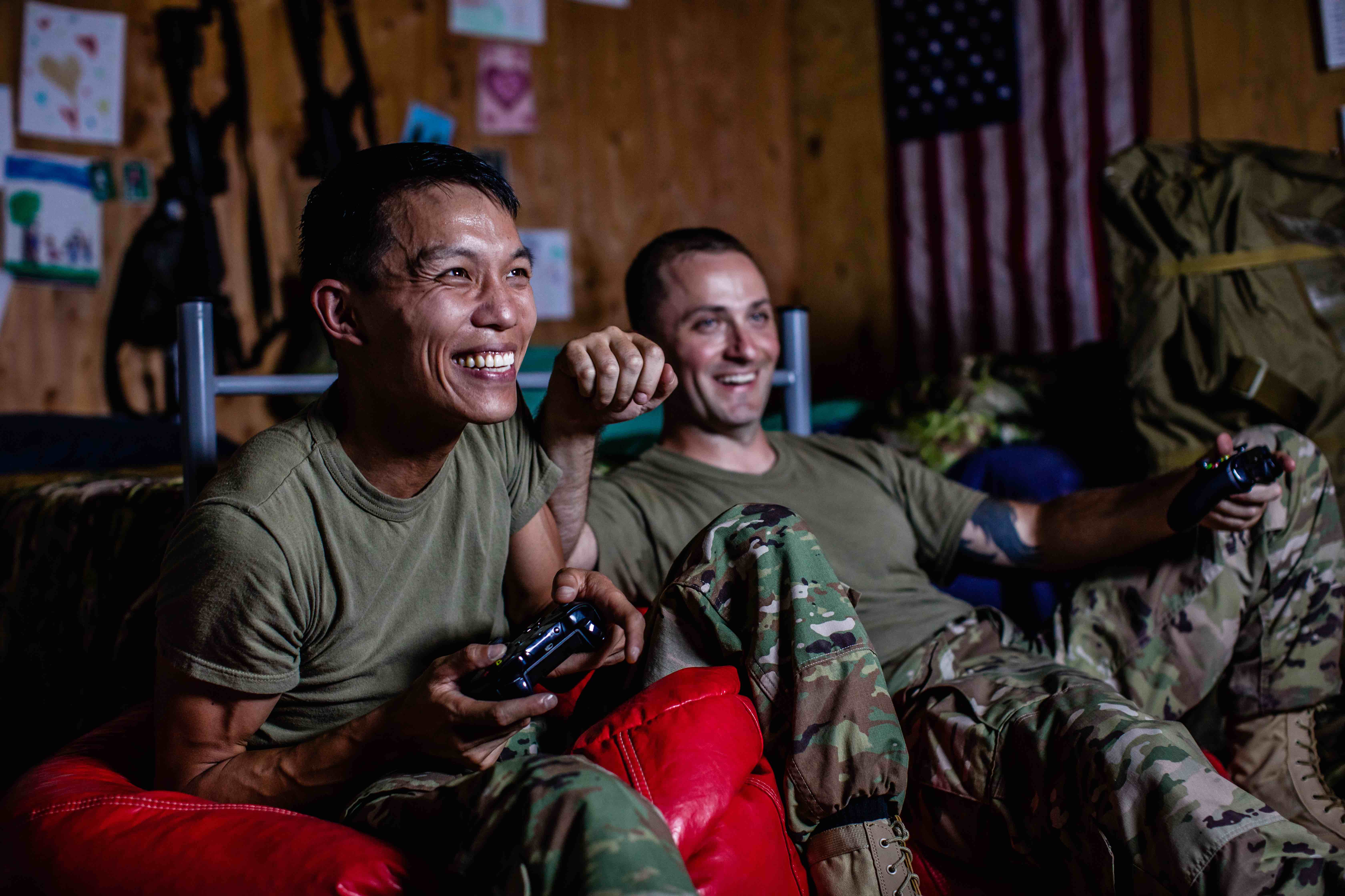 Two military members laugh as they play video games together.