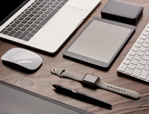 A desk with several electronic devices on it, including a laptop with mouse, an Apple Watch and a tablet